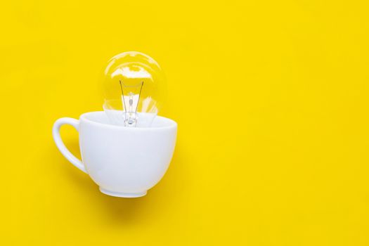  Light bulb in white cup on yellow background. Ideas and creative thinking concept. Copy space