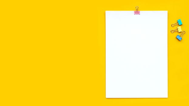 White paper with paperclip on yellow background. Copy space