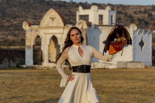 A gorgeous Hispanic Brunette model poses outdoors with a falcon outdoors at a hacienda