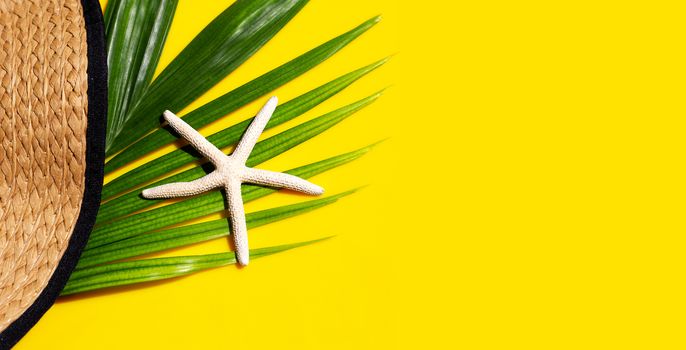 Summer hat with starfish on tropical palm leaves with  on yellow background. Top view