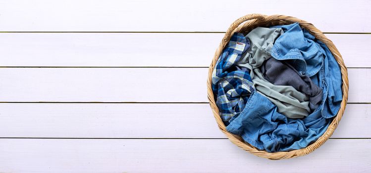 Clothes in laundry basket on white wooden background. Copy space