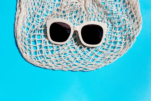 Sunglasses with mesh bag on blue background. Enjoy holiday concept. Copy space