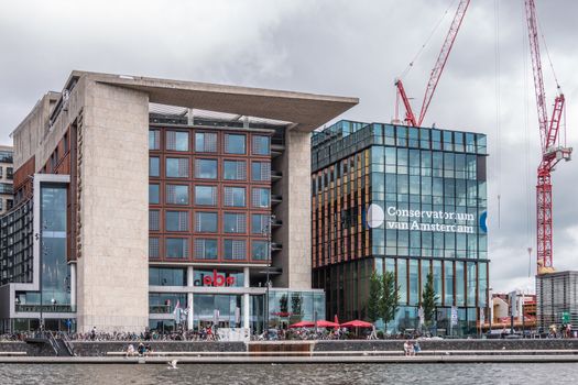 Amsterdam, the Netherlands - July 1, 2019: Library and Conservatorium modern buildings of the city under heavy cloudscape and with red construction cranes on the side.