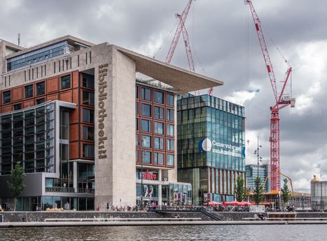 Amsterdam, the Netherlands - July 1, 2019: Library and Conservatorium modern buildings of the city under heavy cloudscape and with red construction cranes on the side.