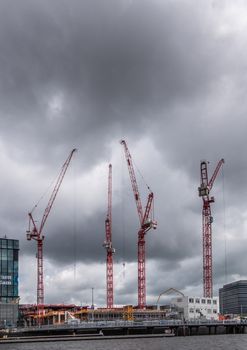 Amsterdam, the Netherlands - July 1, 2019: Construction site with four tall red cranes under heavy rainy cloudscape on Oosterdokskade.