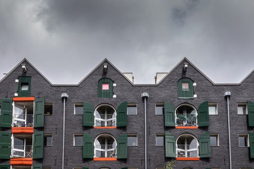 Amsterdam, the Netherlands - July 1, 2019: Gables and facade of warehouse transformed into apartments along canal under heavy cloudscape. Orange and green on black wall.
