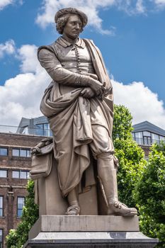 Amsterdam, the Netherlands - July 1, 2019: Beige full body of Rembrandt van Rijn statue on Rembrandtplein under blue sky with white clouds. tall buildings in back.