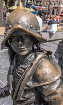Amsterdam, the Netherlands - July 1, 2019: De Nachtwacht compostion of statues on Rembrandtplein. closeup of chest and head of Boy with helmet statue against people and buildings.