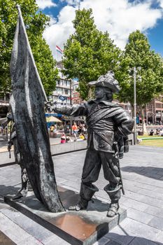 Amsterdam, the Netherlands - July 1, 2019: De Nachtwacht compostion of statues on Rembrandtplein. The Ensign or standard-bearer against green foliage and buidlings. people around.
