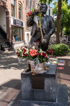 Amsterdam, the Netherlands - July 1, 2019: André Hazes singer songwriter, bronze statue with bouquets of flowers in front, green foliage and housing in back at Albert Cuyp Market.