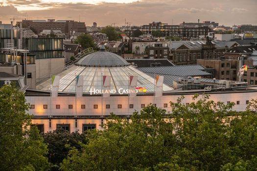 Amsterdam, the Netherlands - July 2, 2019: Daybreak over lighted Holland Casino complex with dome behind Singelgracht park with other buildings in back.