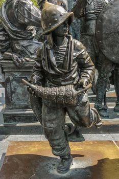 Amsterdam, the Netherlands - July 1, 2019: De Nachtwacht compostion of statues on Rembrandtplein. Full body of Boy with helmet statue against parts of other statues..