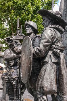Amsterdam, the Netherlands - July 1, 2019: De Nachtwacht compostion of statues on Rembrandtplein. Closeup of body of three soldier figures against green foliage.