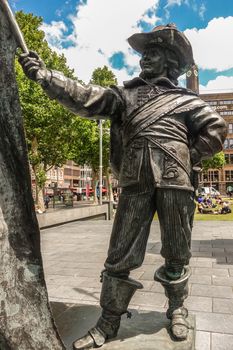 Amsterdam, the Netherlands - July 1, 2019: De Nachtwacht compostion of statues on Rembrandtplein. Closeup of The Ensign or standard-bearer against green foliage and buidlings. people around.