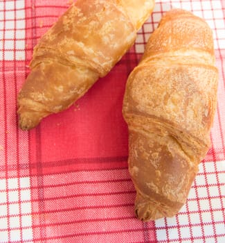 Two fresh croissants lying on a red checkered napkin, top view.