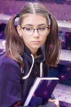 Outdoors portrait of the lovely serious teenage girl holding a book.