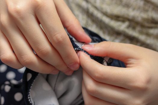 The girl sews with a needle. Needlework. Polka dot fabric