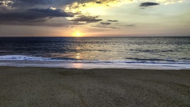 Sunset over the ocean from the shore of Nazaré beach, Playa do Norte, Portugal. The waves break on the shore reflecting the colors of the sky on the wet sand