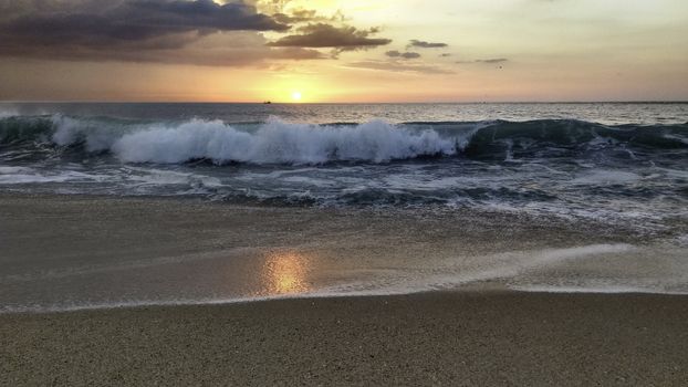 Sunset over the ocean from the shore of Nazaré beach, Playa do Norte, Portugal. The waves break on the shore reflecting the colors of the sky on the wet sand