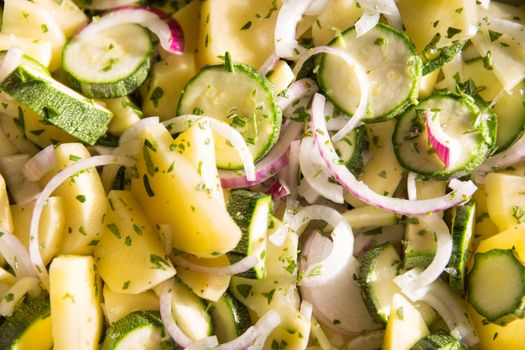 Vegan food: close-up of pan of raw vegetables sliced ​​like ratatouille with courgette, potatoes, onions and seasoned with sage, oregano and rosemary before being cooked