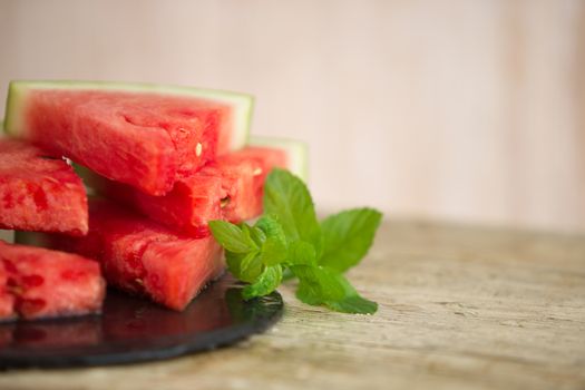 Triangular slices of watermelon overlaid on a black plate of wet slate with sprig of fresh green mint in selective focus for copy space