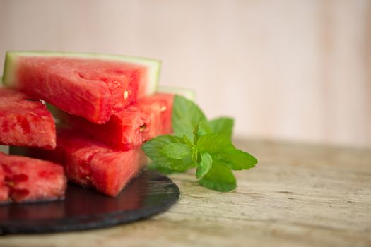 Triangular slices of watermelon overlaid on a black plate of wet slate with sprig of fresh green mint in selective focus for copy space