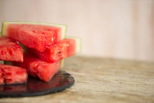 Triangular slices of watermelon overlaid on a black plate of wet slate in selective focus for copy space