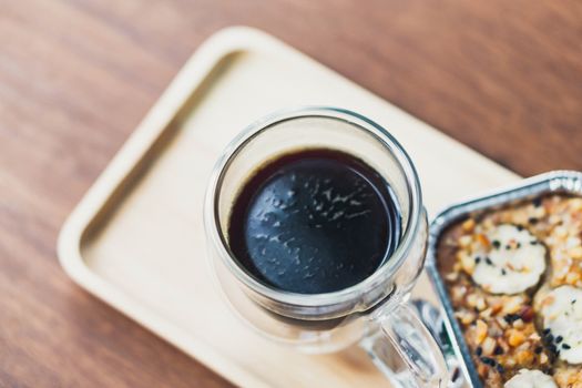 Closeup glass of hot americano coffee and cake on wood table, selective focus, vintage tone