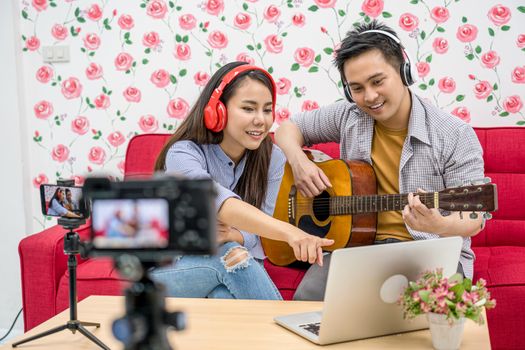 Asian Vlogger of married couple playing and sharing the music to attendee via mobile phone by social media channel,checking comment via laptop, camera taking video and live,vlog and Influencer concept