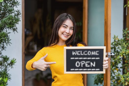 Asian Small business owner hands holding and showing the chalkboard with Welcome Open sign in front of coffee shop, startup with cafe store, installing open and close label concept
