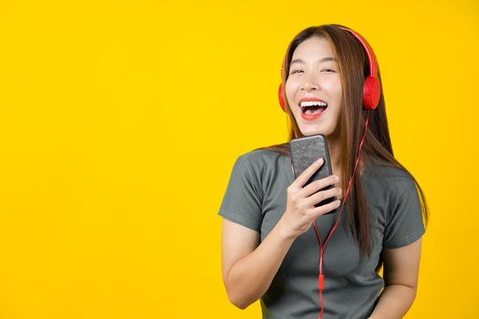 Happiness Asian smiling young woman wearing technology wireless headphones for listening the music via smart mobile phone on isolated yellow color background, Lifestyle and leisure with hobby concept