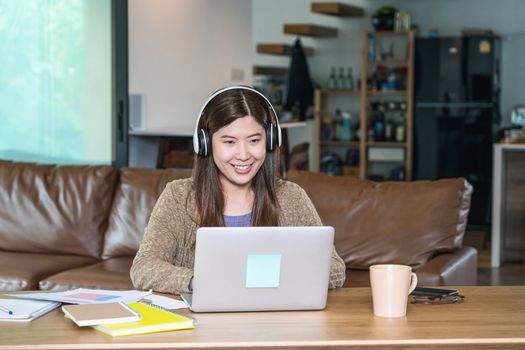 Asian business woman using technology laptop and headphone for working from home in indoor house by video conference call, startups and business owner, social distance and self responsibility