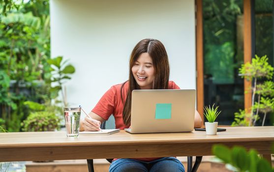 Asian business woman using technology laptop and writing notebook for working from home in outdoor home and garden, startups and business owner, social distance and self responsibility