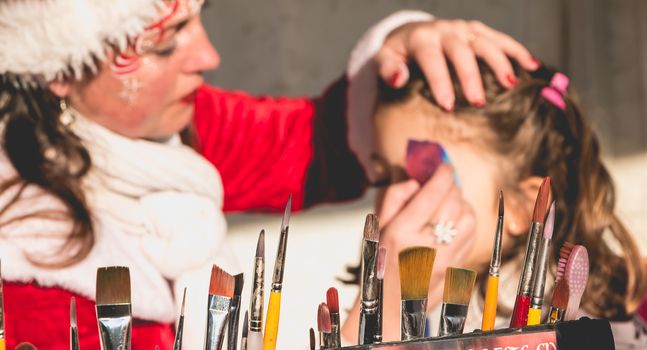 Bretignolles sur Mer, France - December 18, 2016 : During the Christmas period, a little girl is applying makeup in a stand on a Christmas market