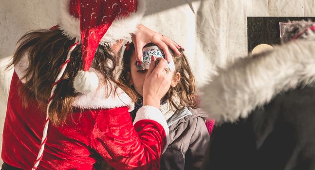 Bretignolles sur Mer, France - December 18, 2016 : During the Christmas period, a little girl is applying makeup in a stand on a Christmas market