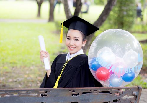 Portrait of happy young female graduates in academic dress and square academic cap holding word quotes of CONGRATS GRAD on balloon after convocation ceremony.