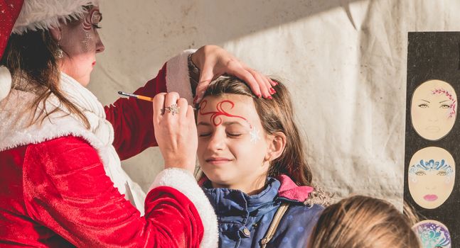 Bretignolles sur Mer, France - December 18, 2016 : During the Christmas period, a little girl is applying makeup in a stand on a Christmas market