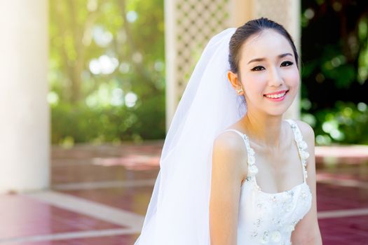 bride is sitting with flowers. Beautiful Young woman posing in park or garden in white bridal dress outdoors on a bright sunny day.