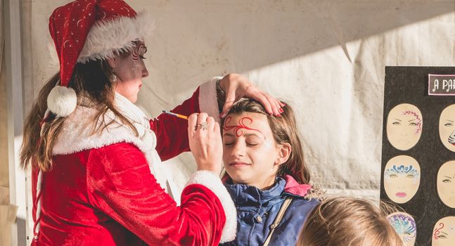 Bretignolles sur Mer, France - December 18, 2016 : During the Christmas period, a little girl is applying makeup in a stand on a Christmas market