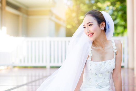 bride is sitting with flowers. Beautiful Young woman posing in park or garden in white bridal dress outdoors on a bright sunny day.