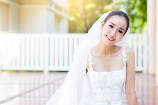 bride is sitting with flowers. Beautiful Young woman posing in park or garden in white bridal dress outdoors on a bright sunny day.