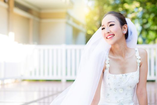 bride is sitting with flowers. Beautiful Young woman posing in park or garden in white bridal dress outdoors on a bright sunny day.