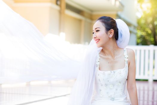 bride is sitting with flowers. Beautiful Young woman posing in park or garden in white bridal dress outdoors on a bright sunny day.