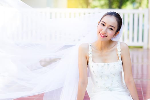 bride is sitting with flowers. Beautiful Young woman posing in park or garden in white bridal dress outdoors on a bright sunny day.