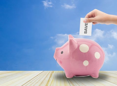 Close up view of the hand of a man placing a paper with save text into the slot of a piggy bank in a savings and investment concept