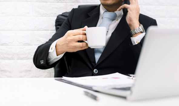 Coffee break businessman executive working relax Hold the phone on laptop at his desk.