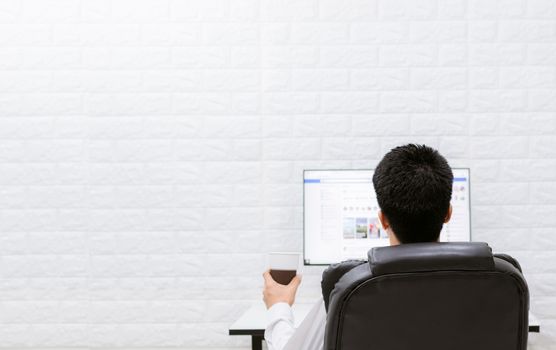 A man happy with a coffee cup watching computers, relaxing at work.