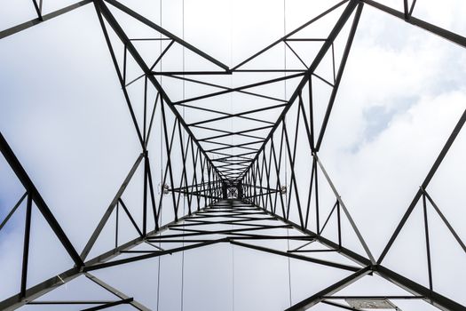 High voltage pylon against cloudy sky. Bottom view. Pattern of metal architecture.