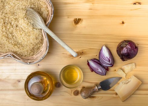 Ingredients for cooking an italian savory meal. Raw parboiled rice, onions, saffron and parmesan over rustic wooden background. Top view. Copy space.