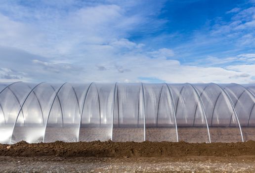 Greenhouse tunnel from polythene plastic on an agricultural field against the blue sky